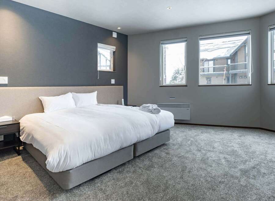 This luxurious bedroom boasts a plush king-size bed, complemented by a neutral color palette and ample natural light from large windows.