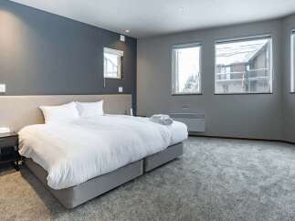 This luxurious bedroom boasts a plush king-size bed, complemented by a neutral color palette and ample natural light from large windows.