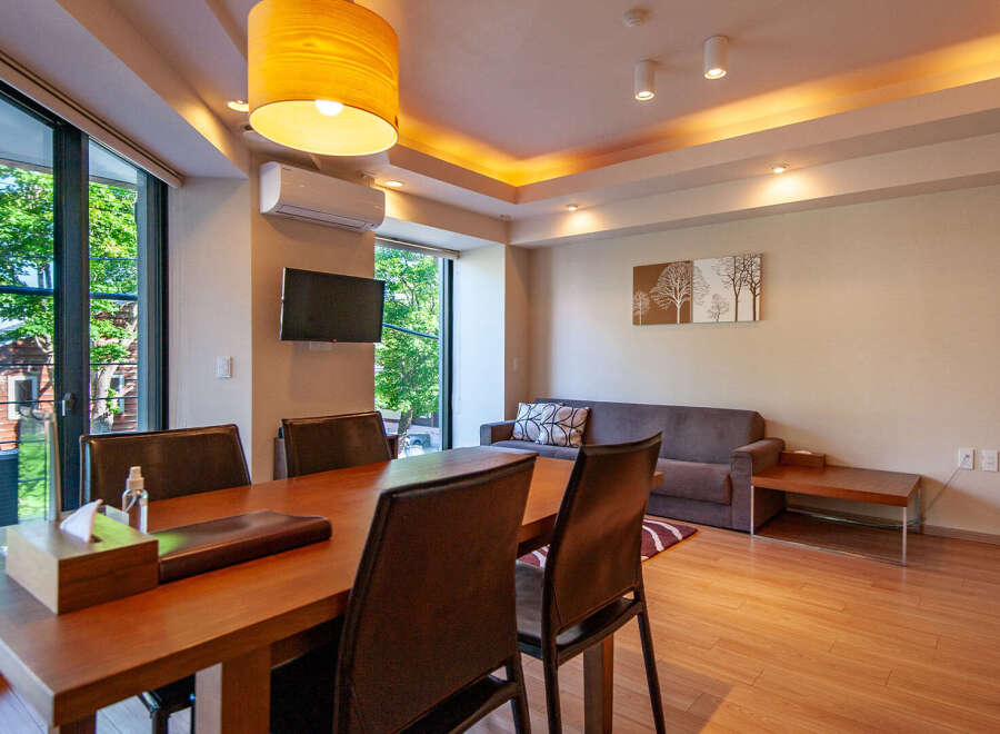 This modern apartment boasts an open-plan living area with hardwood floors, large windows offering scenic views, and a dining table with leather chairs.