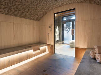 Luxurious spa with a wooden interior, featuring a built-in bench with soft lighting, a glass-enclosed shower, and plush towels.