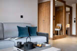 Cozy living room with a grey sofa, teal pillows, and a wooden coffee table featuring a tray with tea set and pastries.