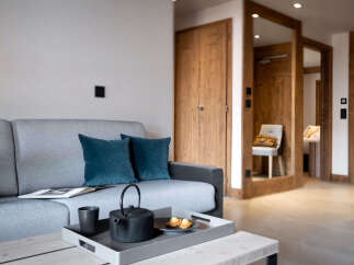 Cozy living room with a grey sofa, teal pillows, and a wooden coffee table featuring a tray with tea set and pastries.