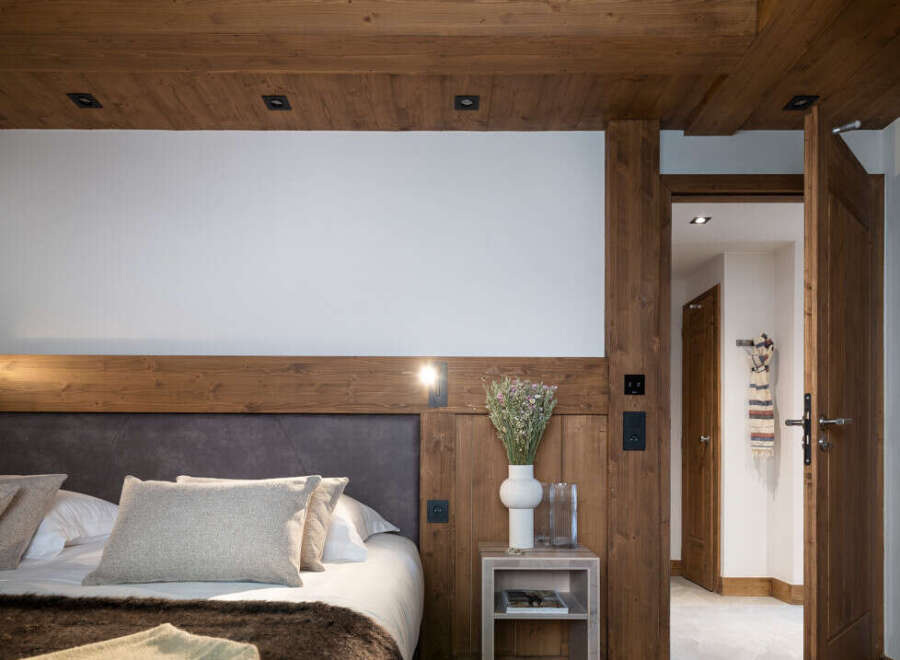 This luxurious bedroom boasts a cozy, rustic-chic design with exposed wooden beams and a plush bed dressed in soft linens.