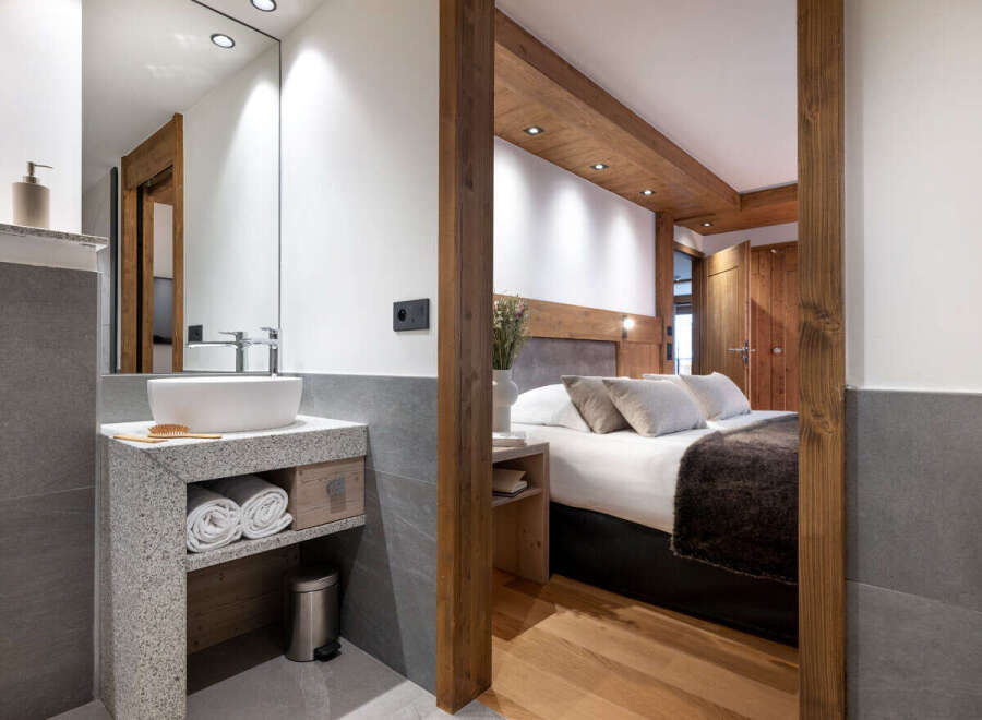 This stunning hotel room boasts a modern bathroom with a granite vanity and a spacious bedroom with a cozy bed and wooden accents.