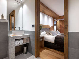 This stunning hotel room boasts a modern bathroom with a granite vanity and a spacious bedroom with a cozy bed and wooden accents.