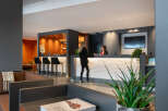 Modern hotel lobby with a stylish reception desk featuring a textured white panel and a built-in bar area with bar stools.