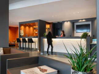 Modern hotel lobby with a stylish reception desk featuring a textured white panel and a built-in bar area with bar stools.