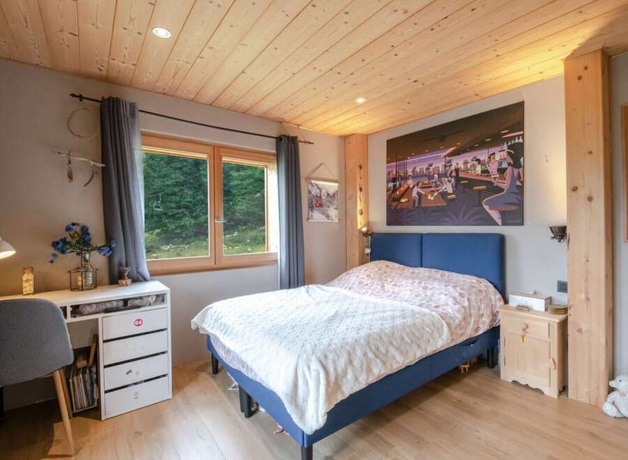 Cozy bedroom with wooden ceiling and large window offering scenic views.