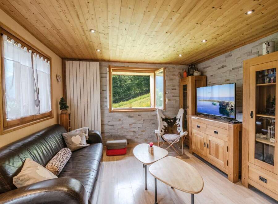 Cozy chalet living room with wooden walls and ceilings, featuring a large leather sofa, a cowhide chair, and a flat-screen TV.