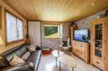 Cozy chalet living room with wooden walls and ceilings, featuring a large leather sofa, a cowhide chair, and a flat-screen TV.