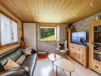 Cozy chalet living room with wooden walls and ceilings, featuring a large leather sofa, a cowhide chair, and a flat-screen TV.