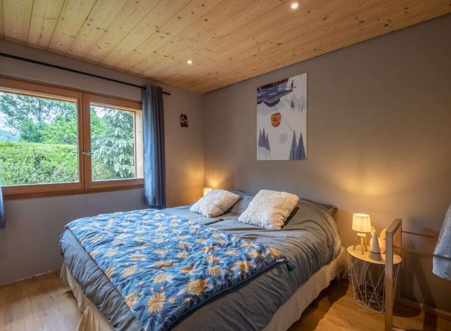 Cozy bedroom with wooden ceiling and large window overlooking a lush green landscape.