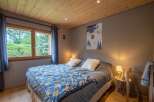 Cozy bedroom with wooden ceiling and large window overlooking a lush green landscape.