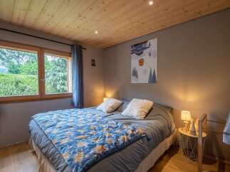 Cozy bedroom with wooden ceiling and large window overlooking a lush green landscape.