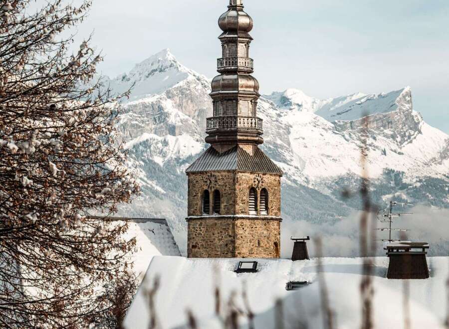 A stunning winter scene unfolds, showcasing a snow-covered church steeple against a backdrop of majestic, snow-capped mountains.