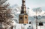 A stunning winter scene unfolds, showcasing a snow-covered church steeple against a backdrop of majestic, snow-capped mountains.