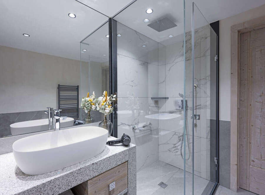 This luxurious bathroom boasts a spacious walk-in shower with glass enclosure and marble tile, complemented by a sleek granite countertop vanity with an oval sink.