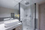 This luxurious bathroom boasts a spacious walk-in shower with glass enclosure and marble tile, complemented by a sleek granite countertop vanity with an oval sink.
