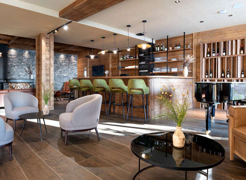 This stunning hotel lobby boasts a chic bar with green velvet stools, a grand piano, and comfortable seating areas.
