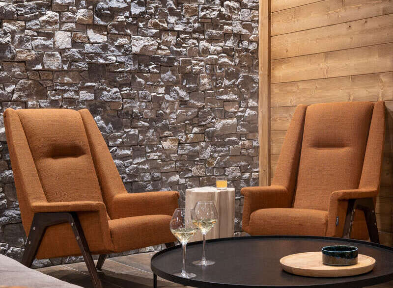 Cozy living room with two orange armchairs facing a black coffee table, featuring a stone accent wall and wood paneling.