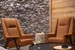 Cozy living room with two orange armchairs facing a black coffee table, featuring a stone accent wall and wood paneling.
