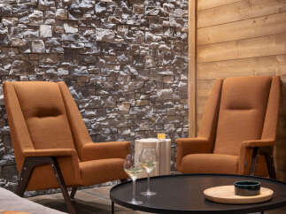 Cozy living room with two orange armchairs facing a black coffee table, featuring a stone accent wall and wood paneling.