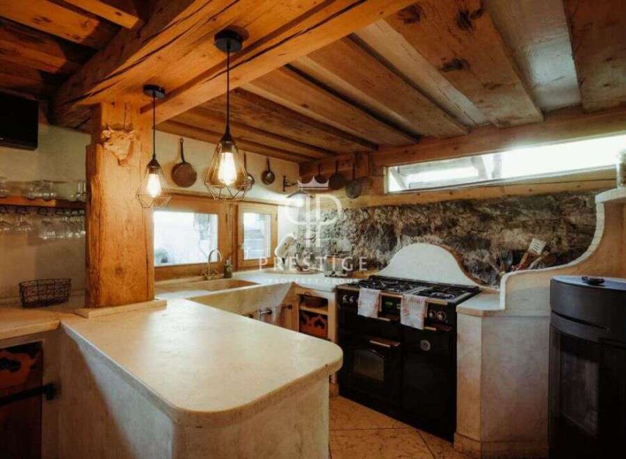 Discover rustic charm in this stunning kitchen! Featuring exposed wooden beams, a stone accent wall, and unique light fixtures, this space exudes warmth and character.