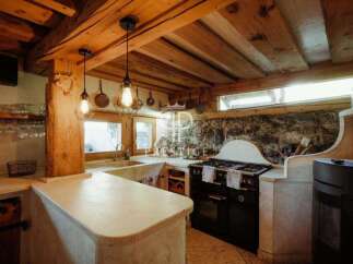 Discover rustic charm in this stunning kitchen! Featuring exposed wooden beams, a stone accent wall, and unique light fixtures, this space exudes warmth and character.