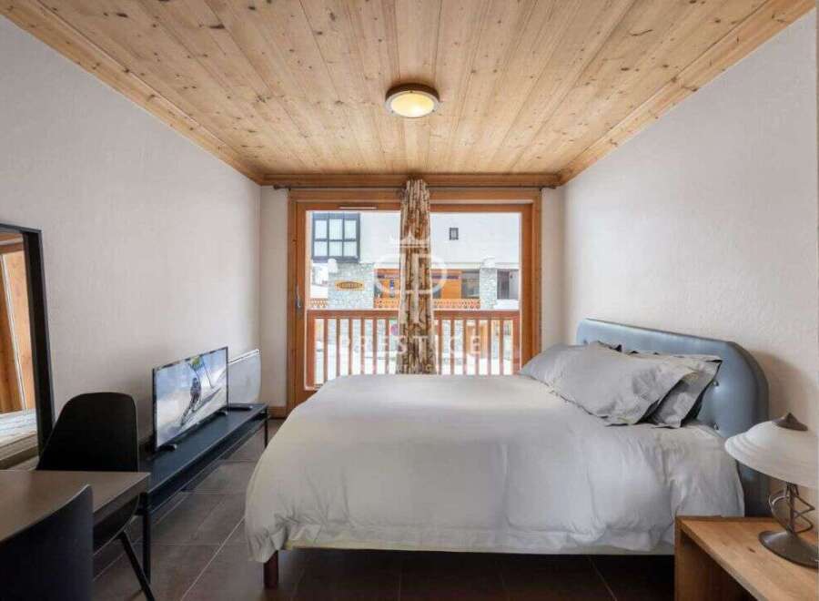 Cozy bedroom with a wooden ceiling and a large window offering natural light.
