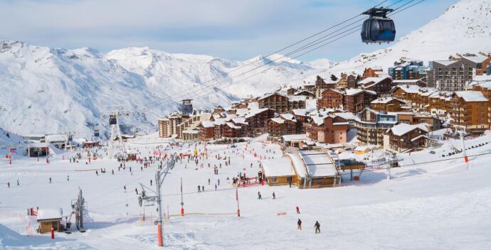 A lively ski resort town nestled in the snowy mountains, with a cable car overhead.