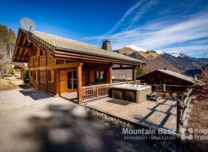 Rustic wooden chalet with a hot tub, set in a scenic mountain landscape.