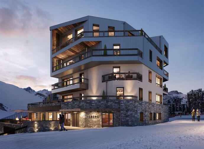 Modern apartment hotel with warm lighting, set in a snowy mountain landscape at dusk.