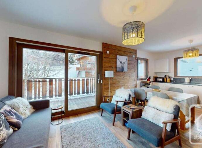Modern chalet living room with cozy seating, a dining area, and large windows overlooking a snowy balcony.