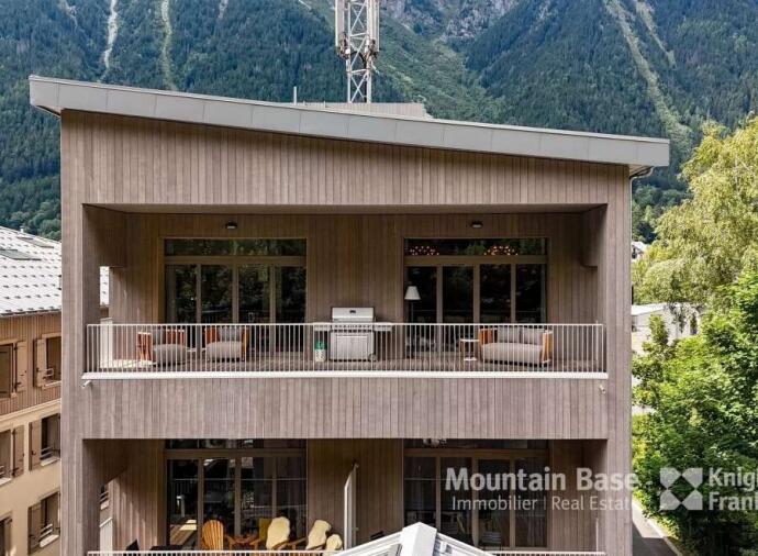 Modern wooden building with balconies, set in green mountain surroundings.