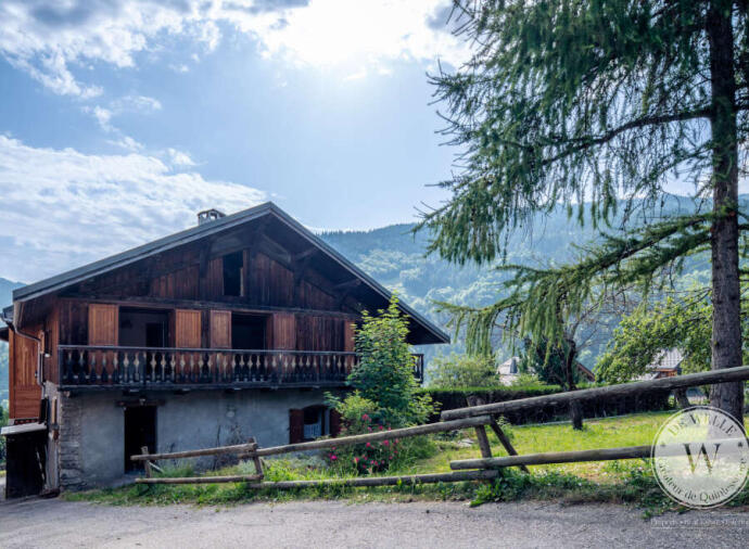 Rustic wooden house with balcony, set in a green mountainous landscape.