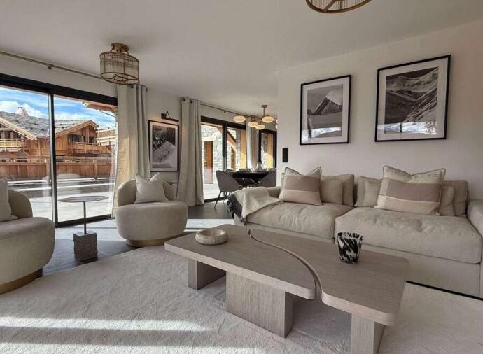 Contemporary chalet living room with neutral sectional sofa, wooden coffee table, and sliding doors to terrace with mountain views