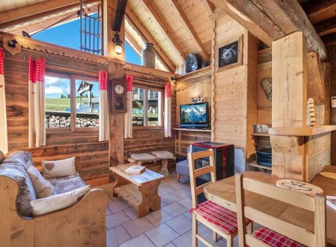 Traditional Alpine chalet interior with wood paneling, exposed beams, red checkered curtains, and rustic wooden furniture