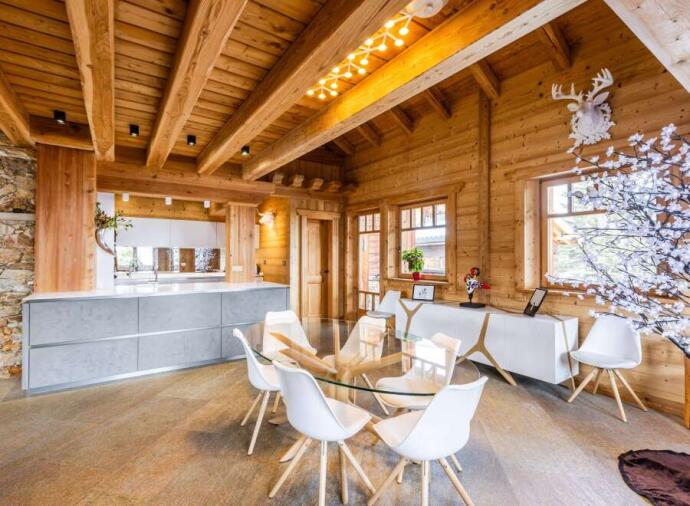 Modern chalet kitchen and dining area with exposed wooden beams, sleek grey cabinets, glass dining table and white chairs