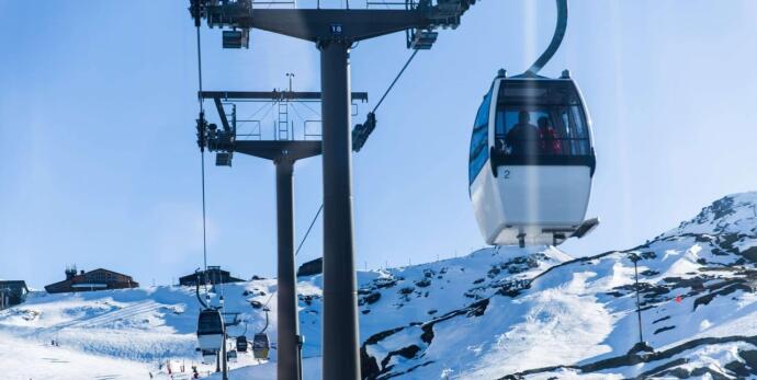 Modern gondola lift operating above snow-covered slopes near Les Gets, with skiers visible below and clear alpine skies overhead.