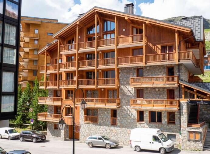 Wooden and stone chalet-style building with balconies and parked cars on a sunny day.