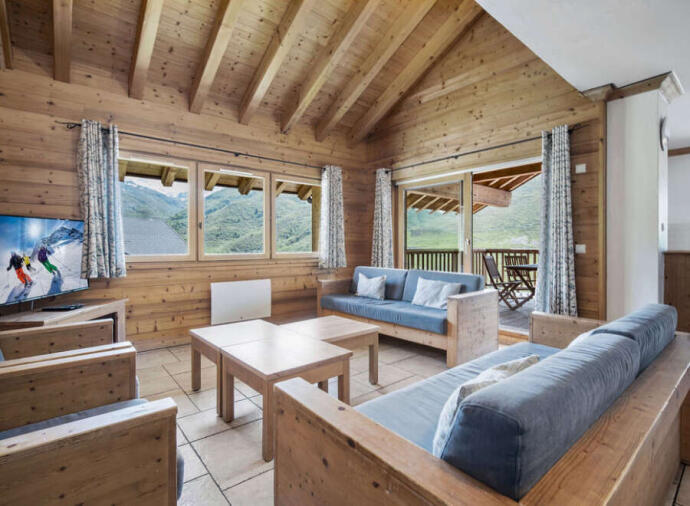 Cozy wooden living room with sofas, coffee table, and mountain views through large windows.