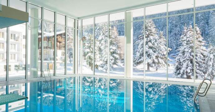 Indoor pool with glass walls overlooking a snowy forest