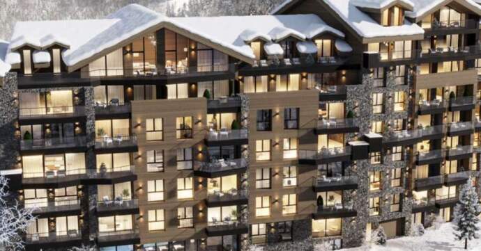 A multi-story apartment building with balconies, surrounded by snow-covered trees and hills, with illuminated windows indicating occupancy.
