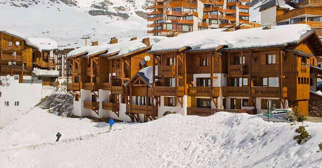 Snow-covered wooden chalets and modern buildings in a mountain ski resort."