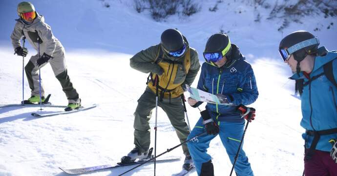 Group of skiers on a snowy slope checking a piste map while paused on the mountain